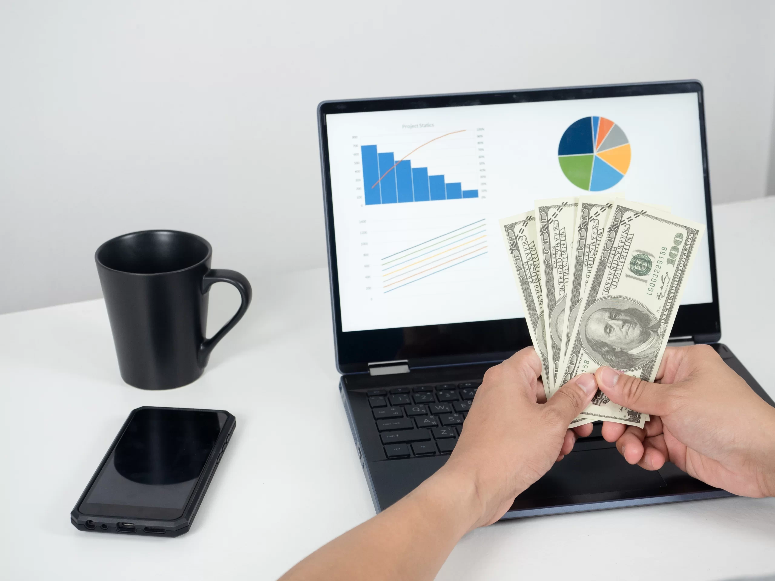 man-hand-holding-money-dollar-and-using-laptop-on-the-table